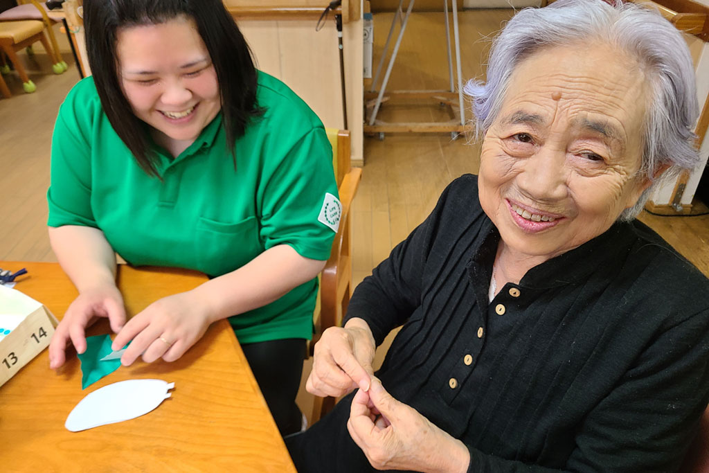 テーブルで折り紙を一緒に折る利用者さんと職員の様子
