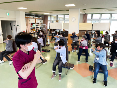 椅子に座って健康体操をする参加者と職員